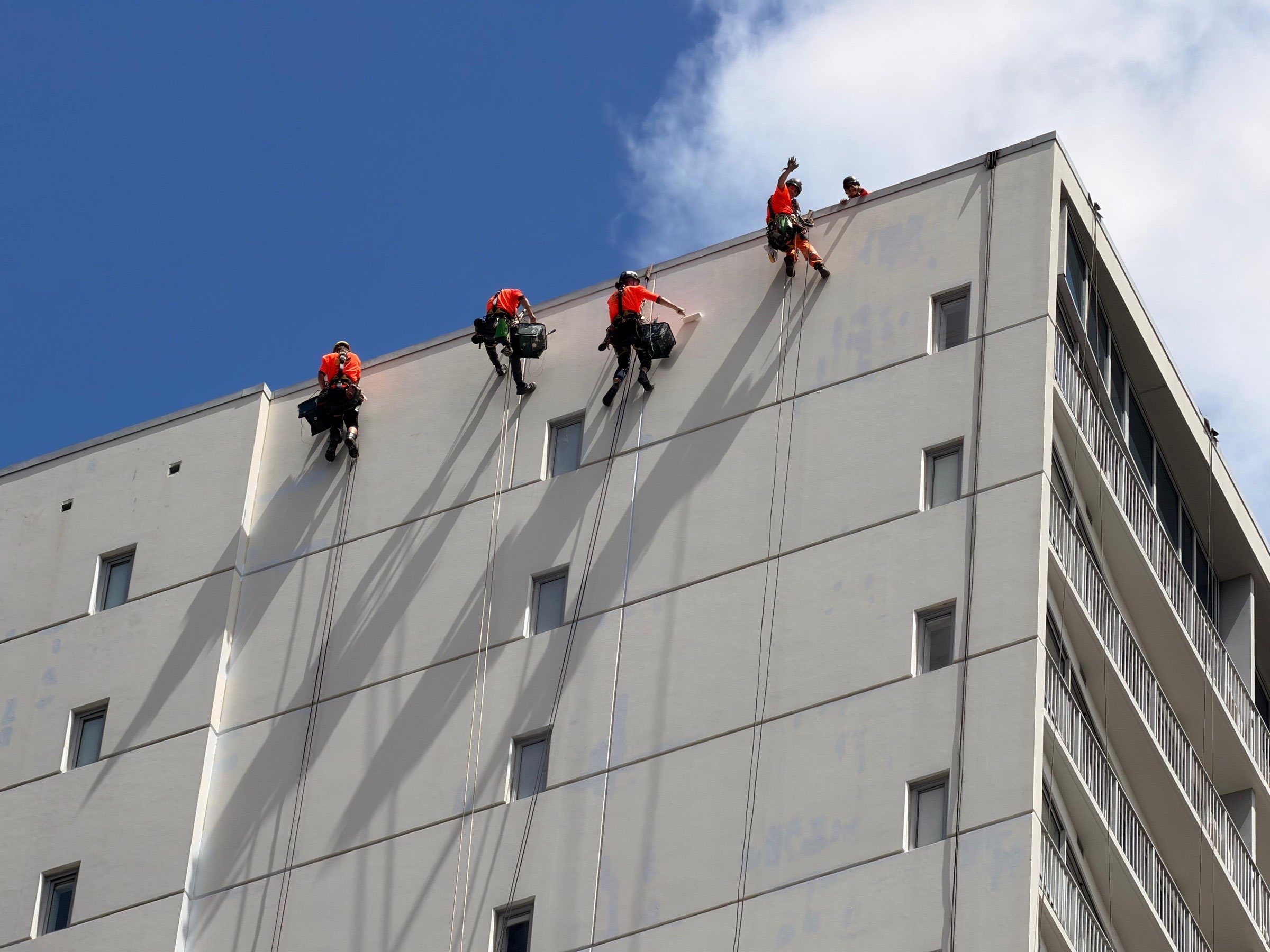 Four On Ropes technicians washing an apartment tower elevation from the rope