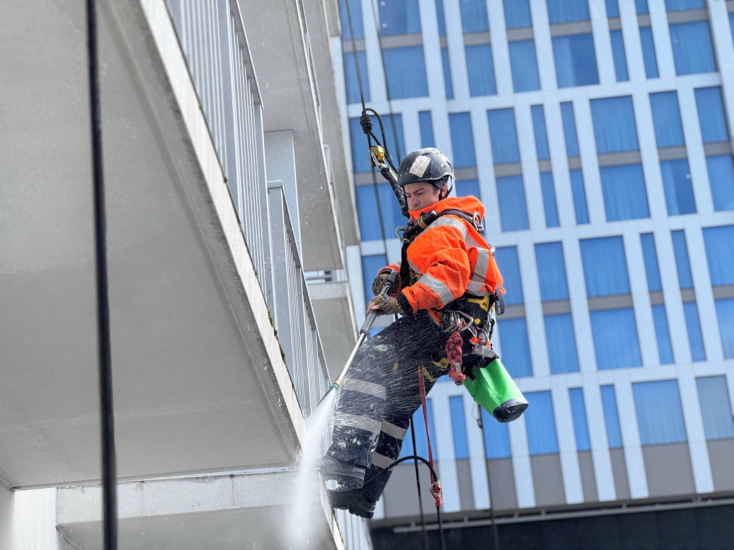 On Ropes technician water-blasting a balcony soffit from the rope