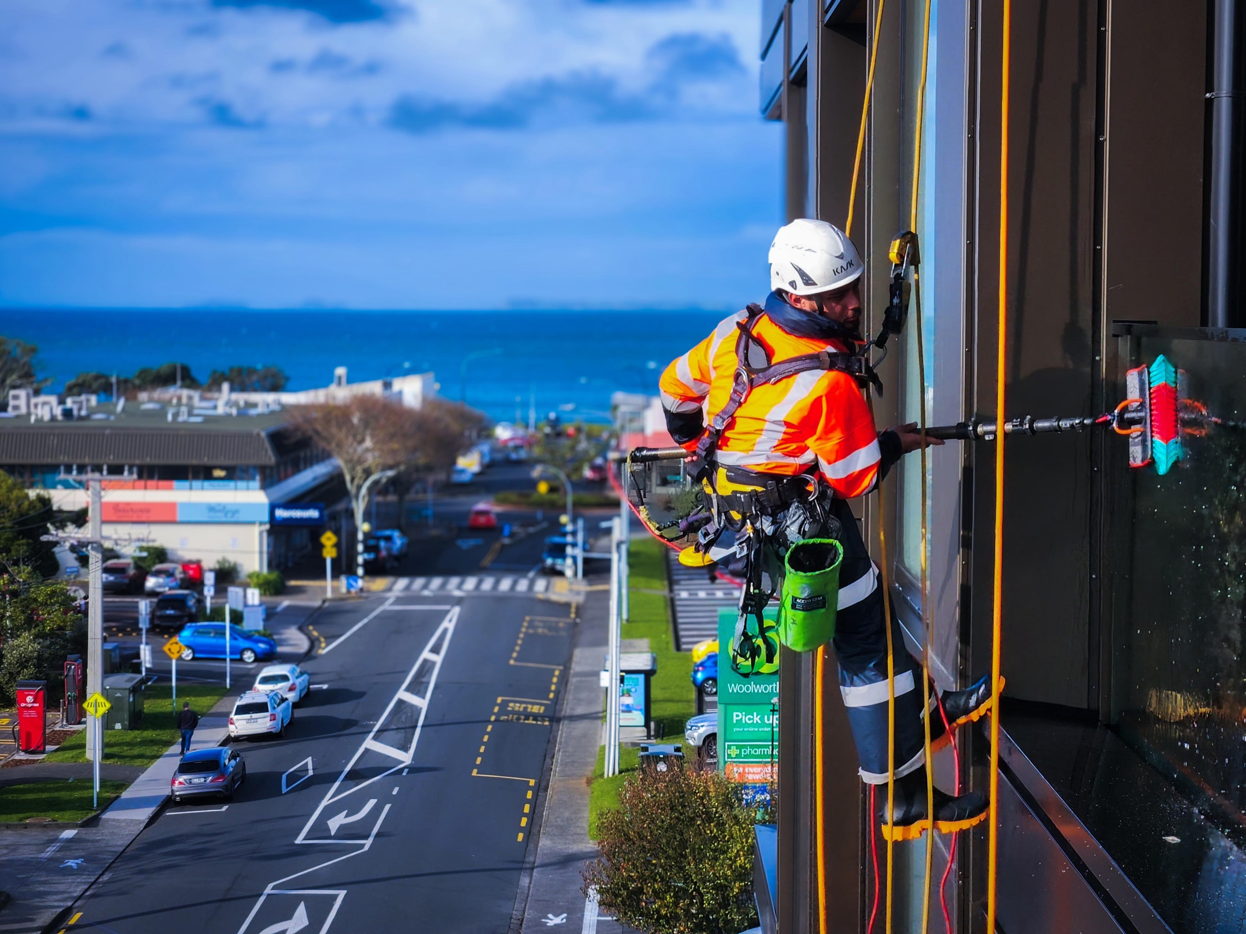 On Ropes technician working on a Takapuna office facade above Hurstmere Road, the Hauraki Gulf behind