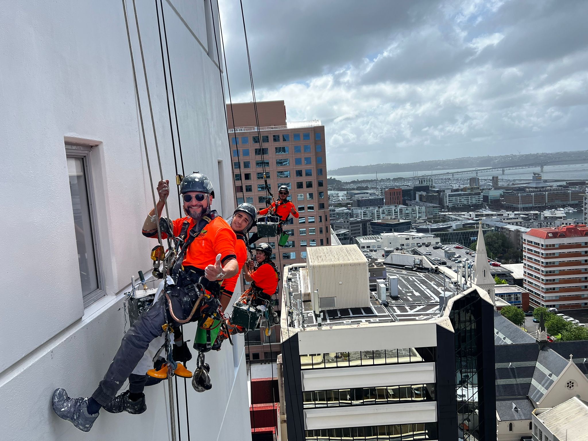 Four On Ropes technicians on ropes down a white tower elevation above the Auckland waterfront