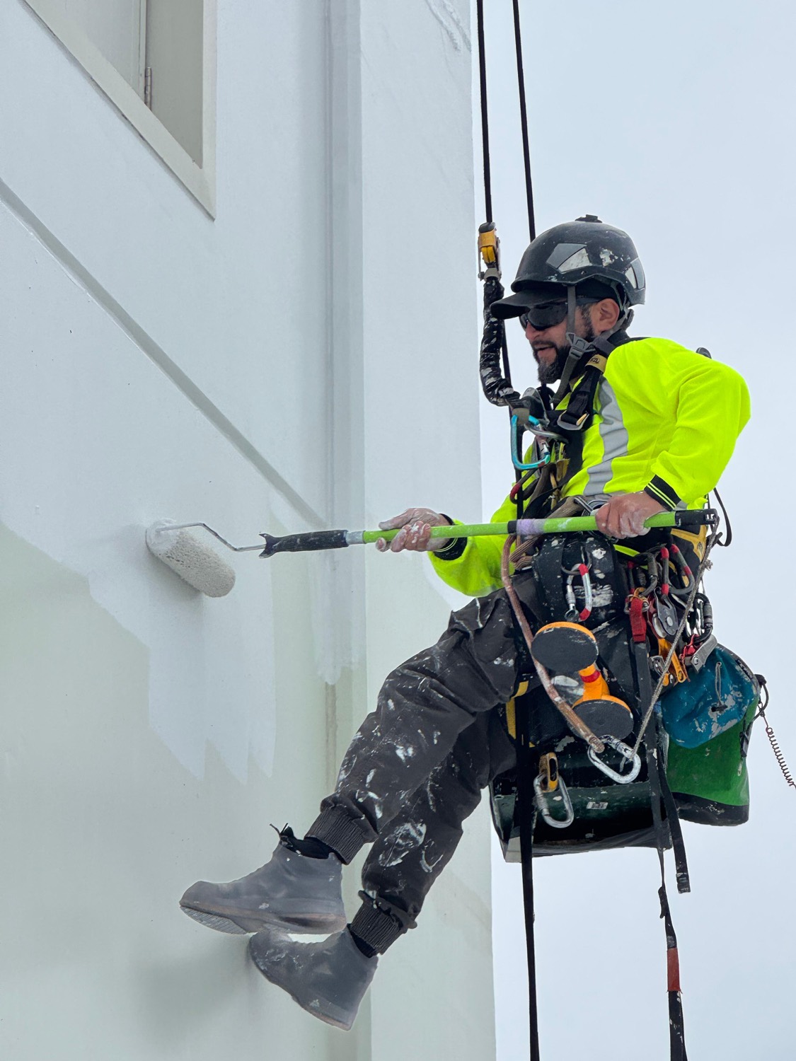 Close detail of an On Ropes technician rolling paint from the rope