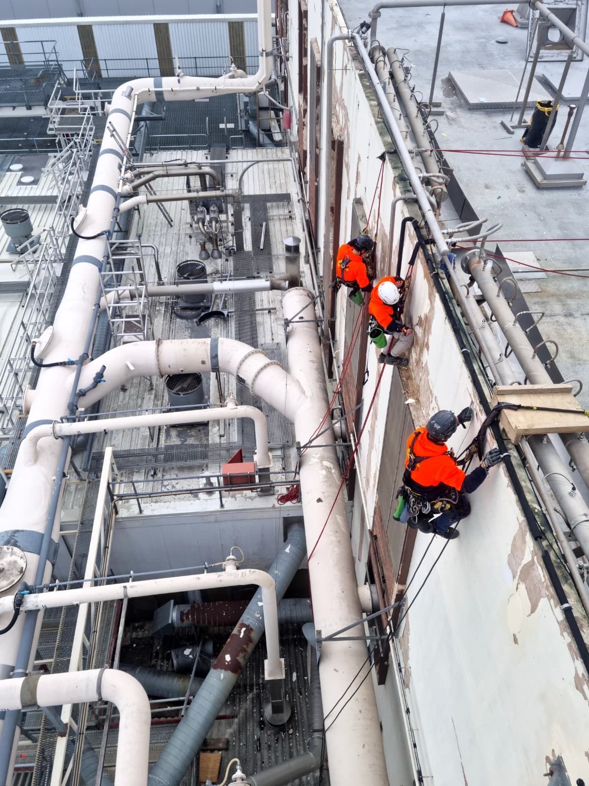On Ropes technicians working an industrial building elevation on ropes above operating plant