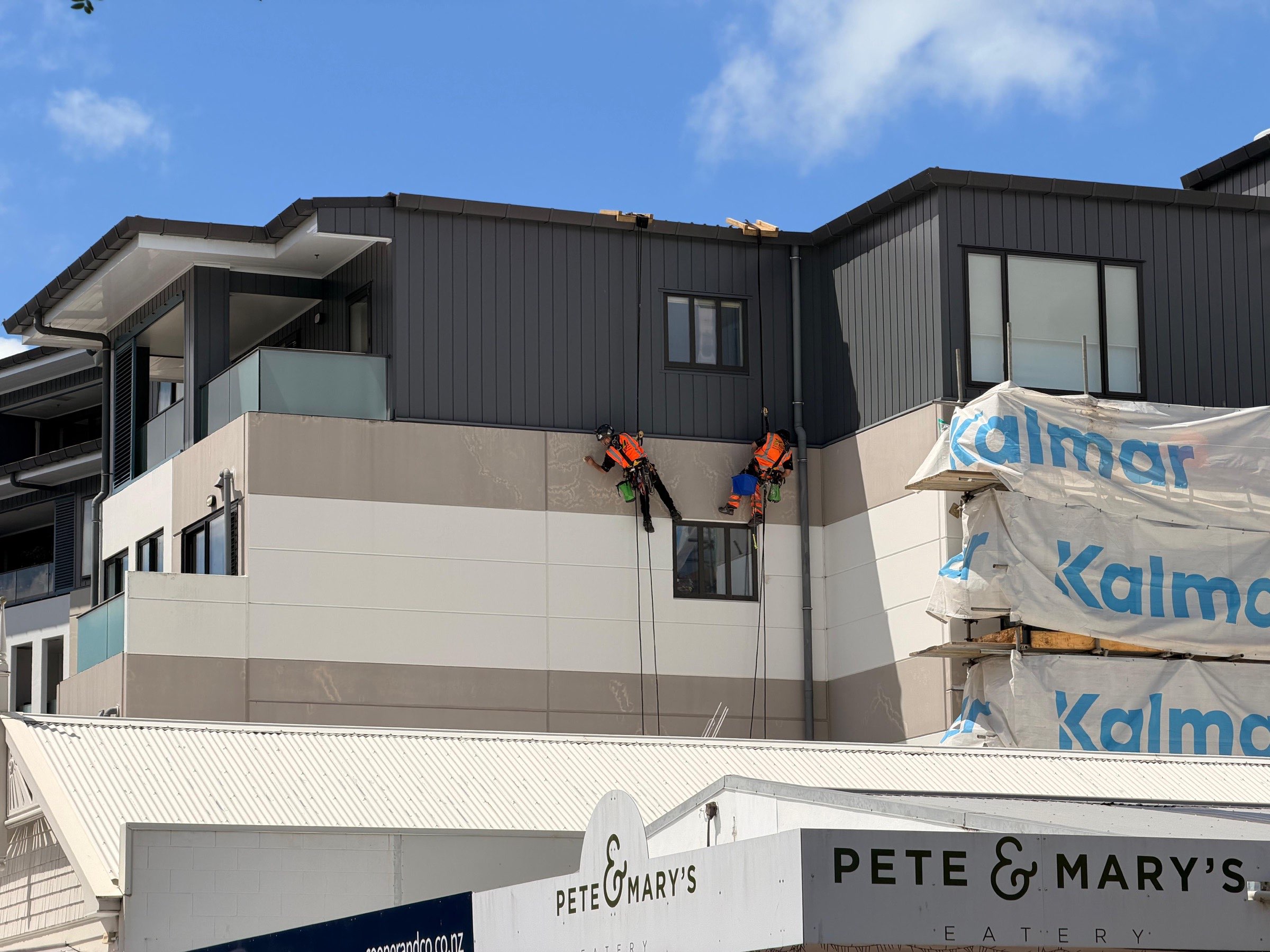 On Ropes technicians on ropes across a wrapped recladding elevation above a retail frontage