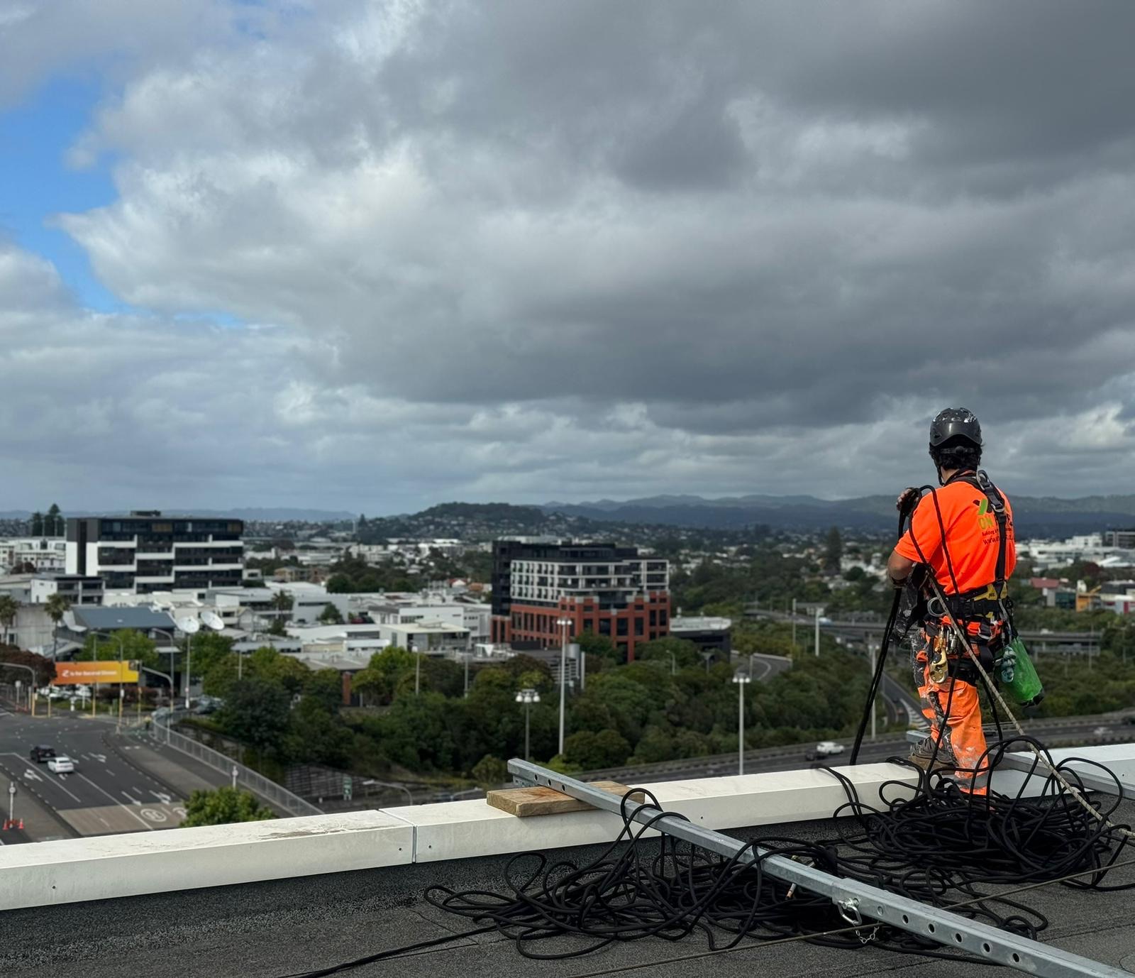 On Ropes technician in full harness beside coiled ropes on an Auckland rooftop