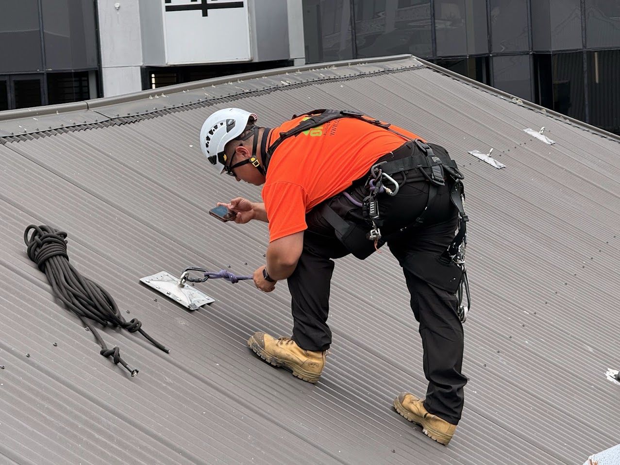 On Ropes technician clipping a line into a roof anchor point and recording it on a phone