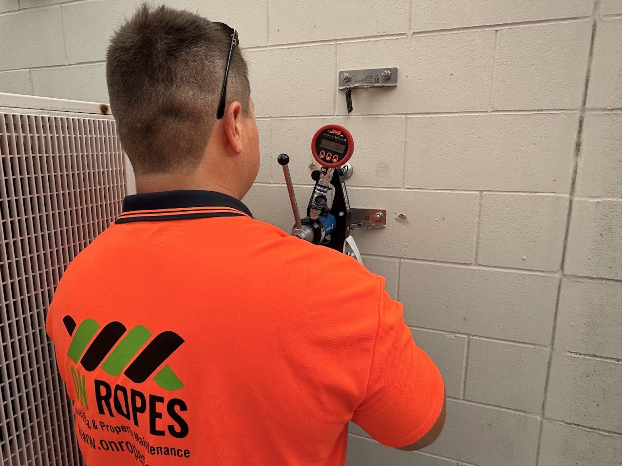 On Ropes technician proof loading an anchor point with a digital load gauge