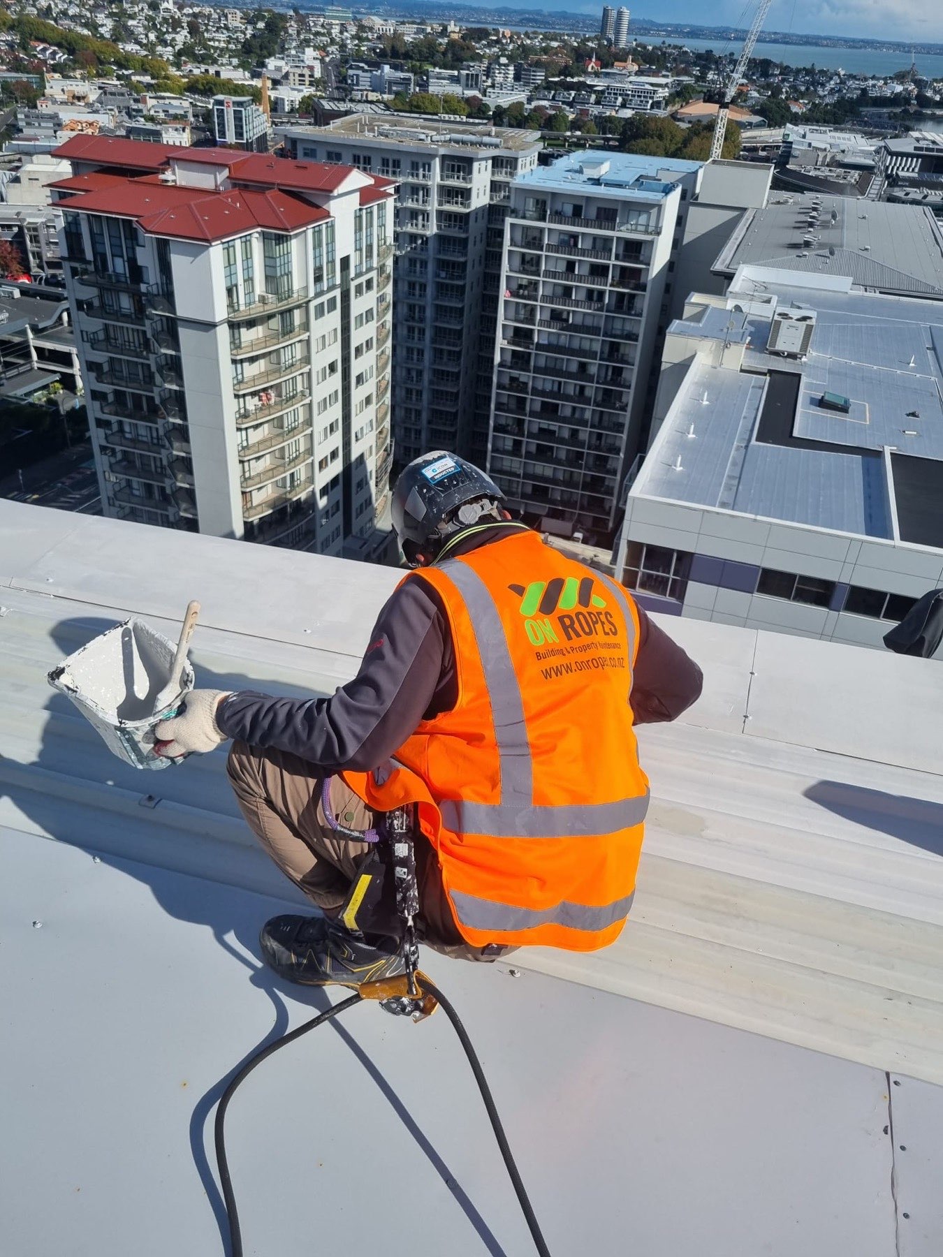On Ropes technician bolting a fixing at a roof edge, harness clipped to the line