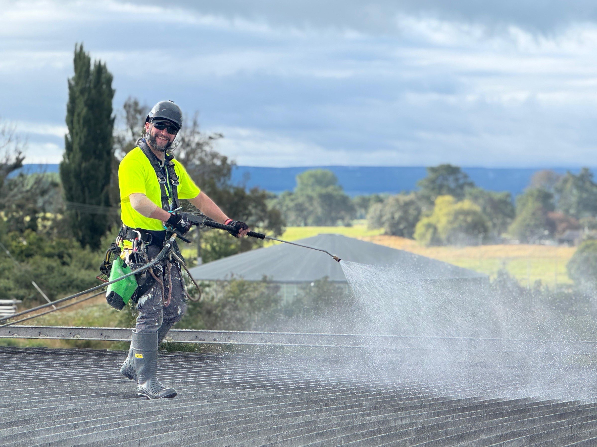 On Ropes technician soft-washing a long roof with a spray lance