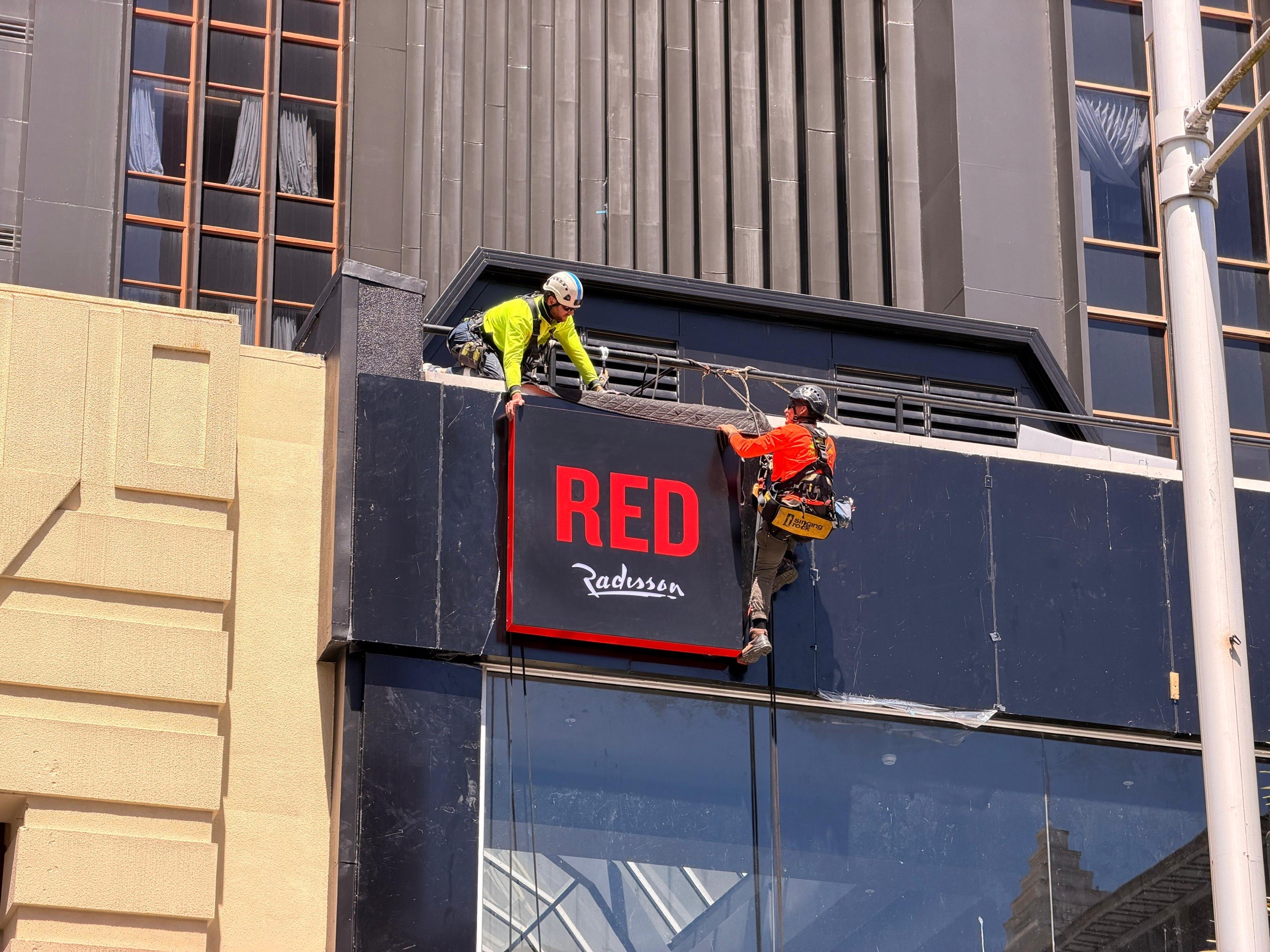 On Ropes technicians installing signage from ropes on a building parapet