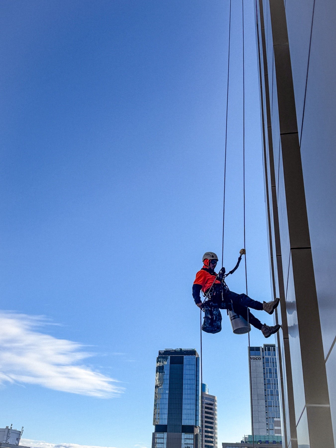 On Ropes technician abseiling on twin ropes mid-elevation against a clear sky