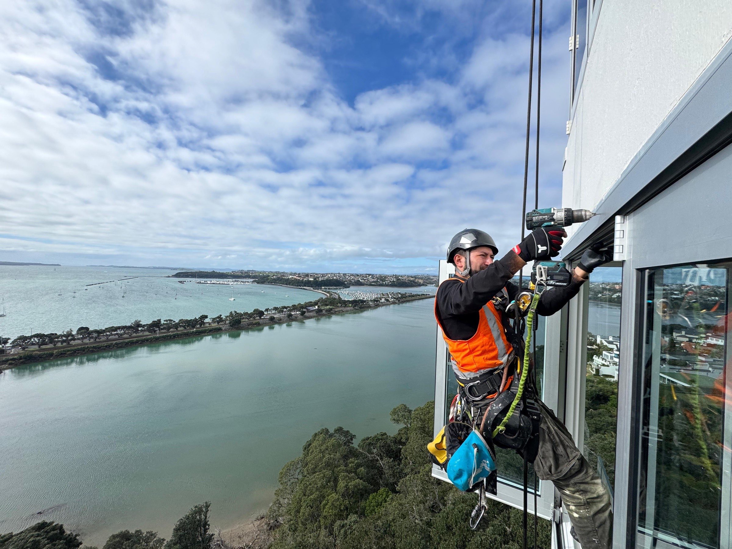 On Ropes technician drilling into window joinery from the rope, high above a tidal harbour